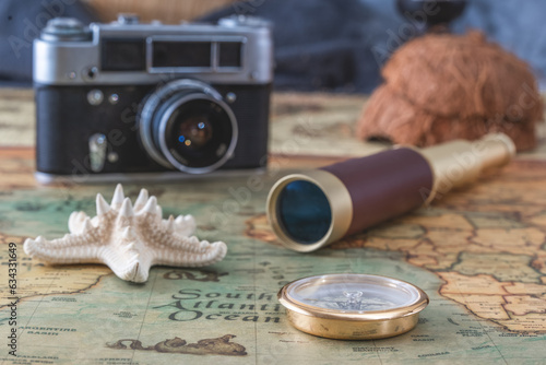 brass compass, a spyglass and a starfish lie on an old map against the background of a vintage film camera