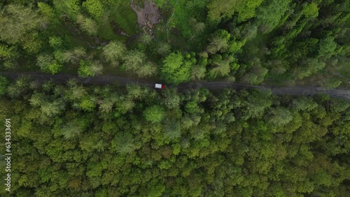 drone footage of a jeep traveling on a track between trees and mountains