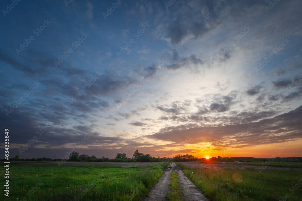 Sunset and evening clouds over meadow with dirt road
