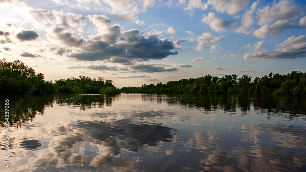 Landscape of a cloudy sky near sunset reflected in the water of the Mississippi River with tree lined banks near Alton, IL
