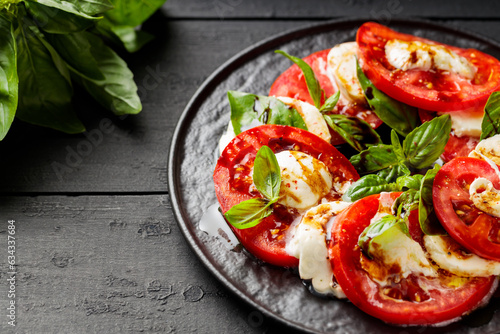 Delicious caprese salad with ripe tomatoes, mozzarella cheese and fresh basil leaves on dark wooden boards. Close up photo