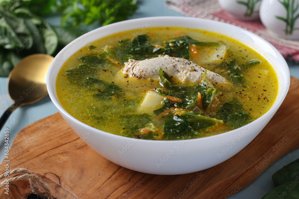 Soup with chicken, spinach and egg in a white bowl on a wooden board Soup with chicken, spinach and egg in a white bowl on a wooden board