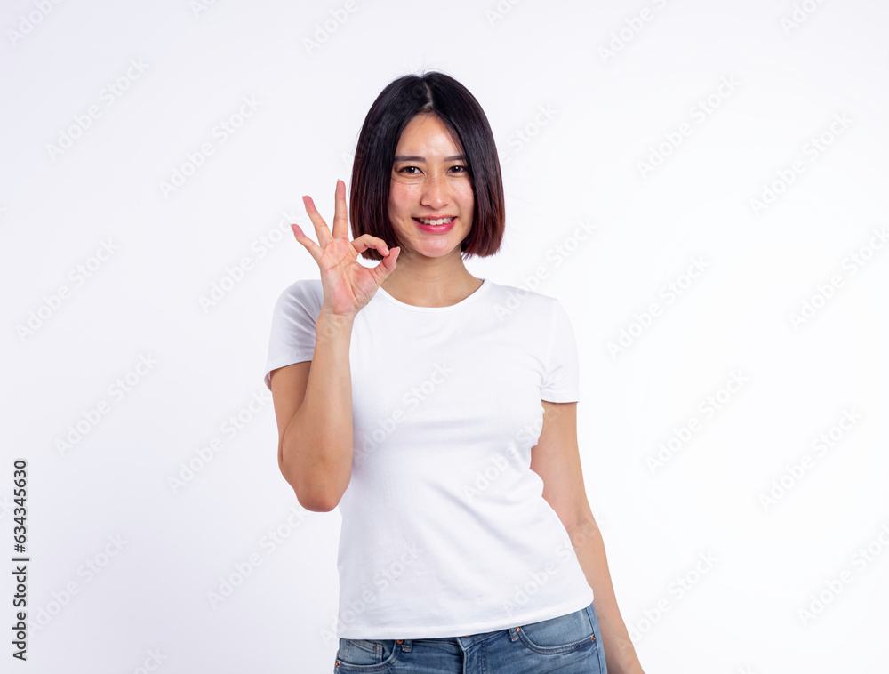 Young woman of asian smiling face in white t-shirt and stand isolated shows ok sign and looking at the camera on white background, she is smiling lifesty, Portrait concept... Young woman of asian smiling face in white t-shirt and stand isolated shows ok sign and looking at the camera on white background, she is smiling lifesty, Portrait concept...