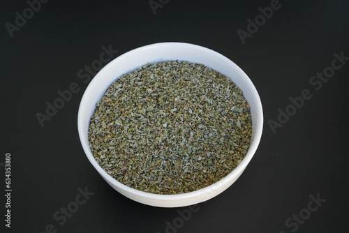 dried oregano in a white plate on a black background