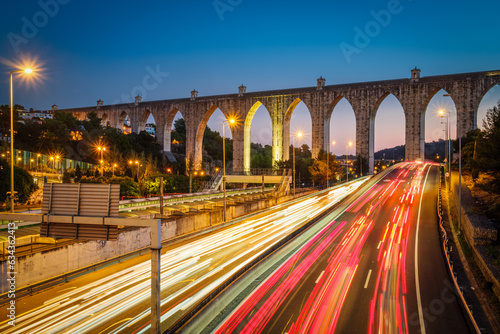 View of highway traffic near Campolide station with Aguas Livres Aqueduct in background in the evening with car lights trails. Lisbon, Portugal photo