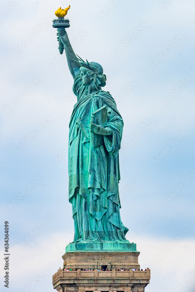 Fototapeta premium New York, New York, United States. August 07, 2023. Dramatic and detailed image of the Statue of Liberty with strong shades of green, sky with many clouds and very high resolution.