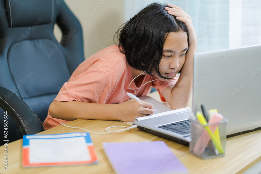 Young Asian girl is bored while doing homework on vacation online with laptop in front of her and plugged in headphones to communicate with friends. Young Asian girl is bored while doing homework on vacation online with laptop in front of her and plugged in headphones to communicate with friends.