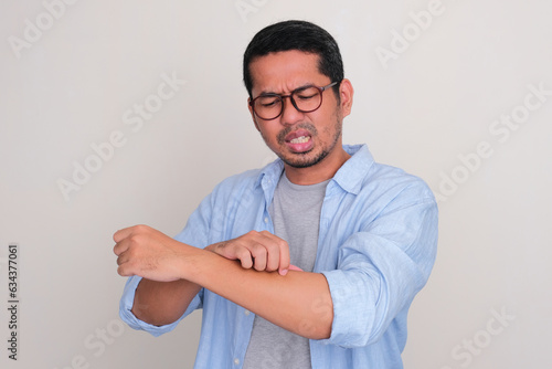 Adult Asian man scratching his hand and showing uncomfortable expression photo