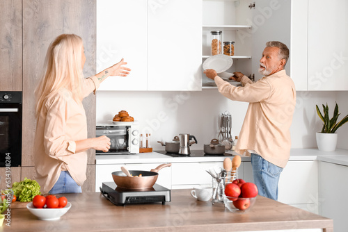 Mature woman and her husband taking plates in kitchen
