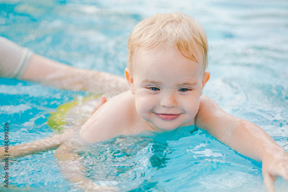 Portrait of small red-haired boy bathes in pool with hand support, baby swimming in water, summer leisure Portrait of small red-haired boy bathes in pool with hand support, baby swimming in water, summer leisure