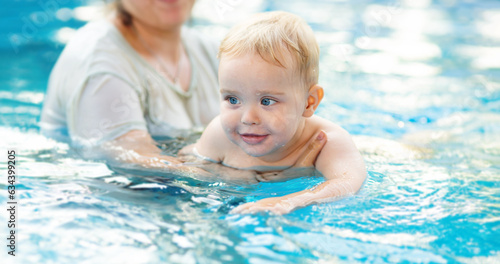 Portrait of small red-haired boy bathes in pool with hand support, baby swimming in water, summer leisure © fantom_rd