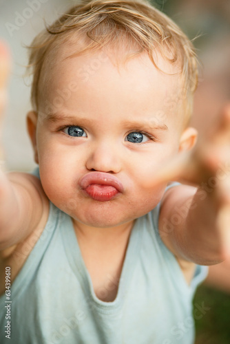small boy with blond hair and blue eyes on nature, child stretching hands into the camera, baby face with funny emotions
