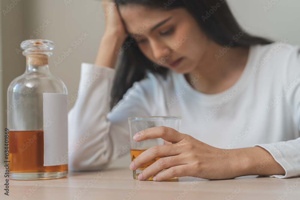 Alcoholism drunk asian young woman hand holding glass of alcohol or whiskey, female sitting alone, drinking on table at home, at night. Treatment of alcohol addiction, suffer abuse problem alcoholism Alcoholism drunk asian young woman hand holding glass of alcohol or whiskey, female sitting alone, drinking on table at home, at night. Treatment of alcohol addiction, suffer abuse problem alcoholism
