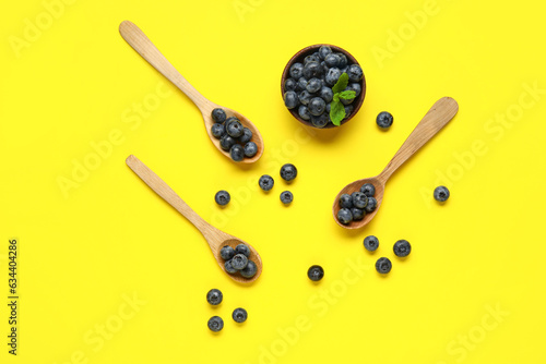 Wooden spoons and bowl with fresh blueberries on yellow background