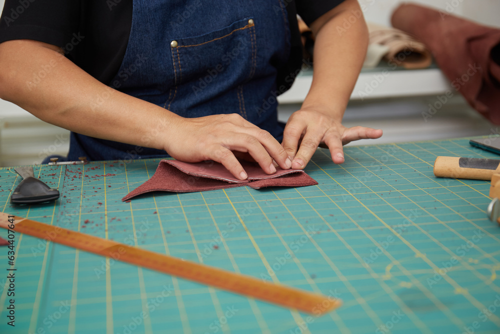 Hand close up of Asian Female leather worker working with tool and a piece of leather Hand close up of Asian Female leather worker working with tool and a piece of leather