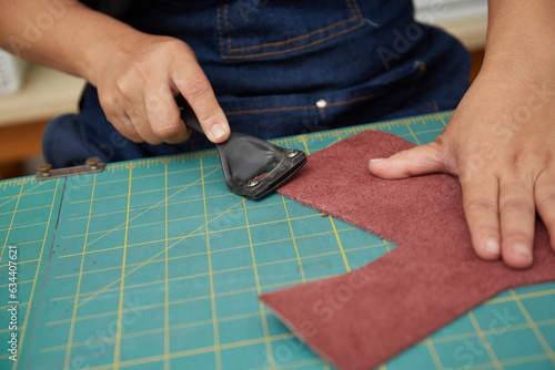 Hand close up of Asian Female leather worker working with tool and a piece of leather 