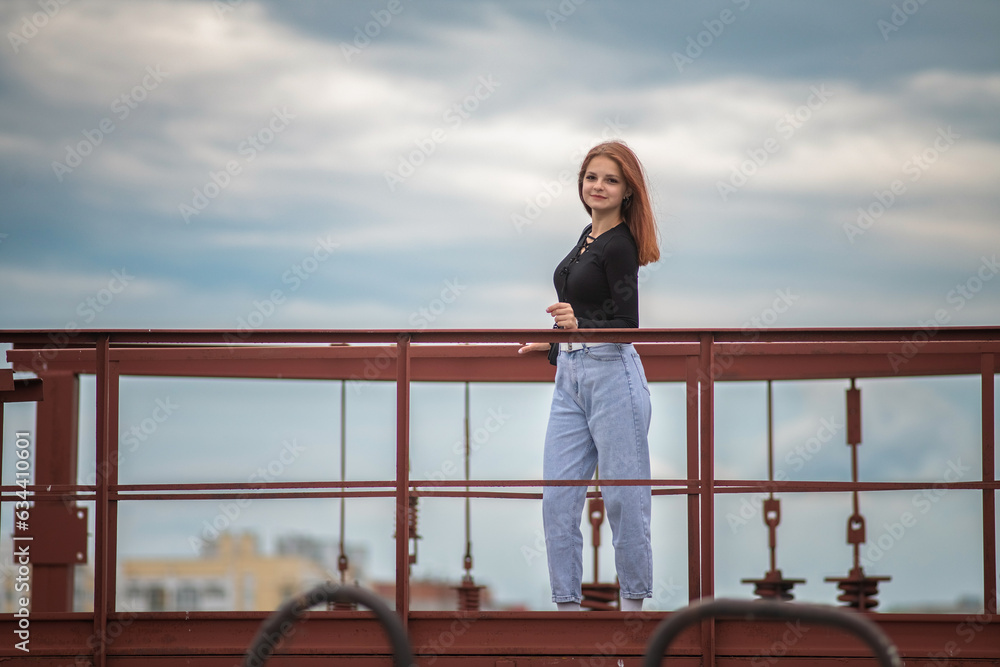 Portrait of a beautiful young girl in jeans and a dark jacket against the background of clouds. Portrait of a beautiful young girl in jeans and a dark jacket against the background of clouds.