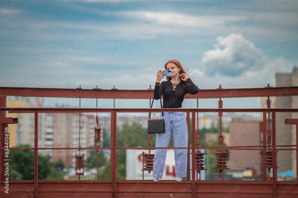 Portrait of a beautiful young girl in jeans and a dark jacket against the background of clouds.