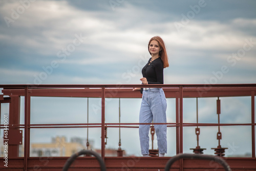 Portrait of a beautiful young girl in jeans and a dark jacket against the background of clouds.