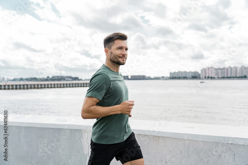 Runner trainer in fitness clothes T-shirt.  A confident male athlete training does warm-up exercises. Jogging in the afternoon in the city.