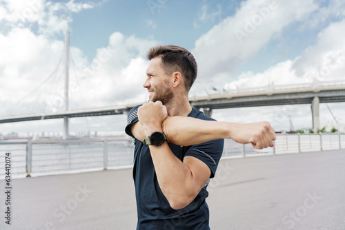 A confident strong man. Runner trainer in fitness clothes T-shirt, running sports shoes and smart watch. Motivation a male athlete training does warm-up exercises.