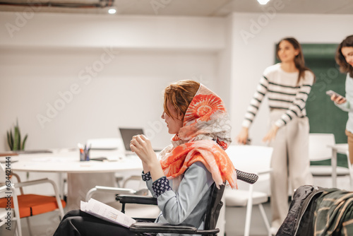 Woman wearing hijab in wheelchair discussing with colleagues at work in a good working atmosphere