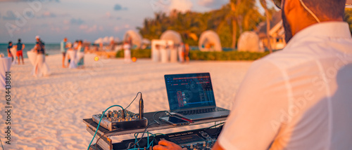Fototapeta Naklejka Na Ścianę i Meble -  Dj mixing at sunset beach party in summer vacation outdoors. Beach sunset party, playing music for tourist people in bar fun concept. Maldives resort panorama, leisure lifestyle