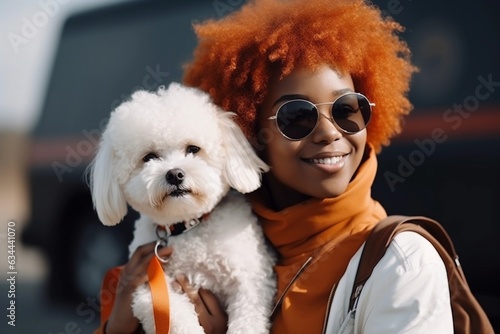 Happy young African American woman is holding her Bichon Frise dog on her hands and walking in the street