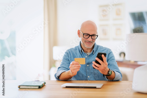 Man sitting at home and using credit card and smartphone and paying online