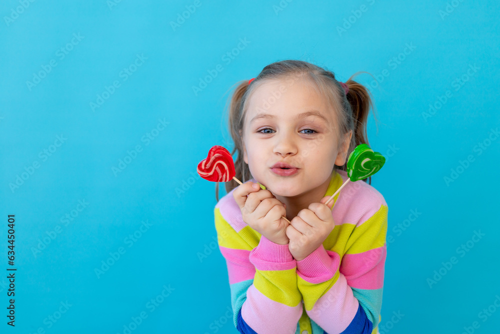 portrait of a joyful little girl with lollipops in a striped jacket, a large candy on a stick. The concept of sweets and confectionery. Blue background, photo studio, place for text portrait of a joyful little girl with lollipops in a striped jacket, a large candy on a stick. The concept of sweets and confectionery. Blue background, photo studio, place for text