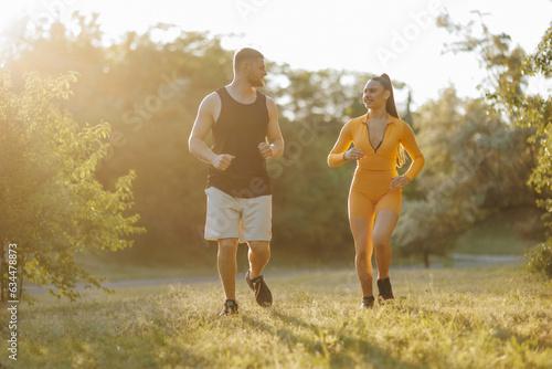A dedicated personal trainer, a young man, is actively coaching and motivating a sportswoman, a female athlete, during their invigorating outdoor jogging session.