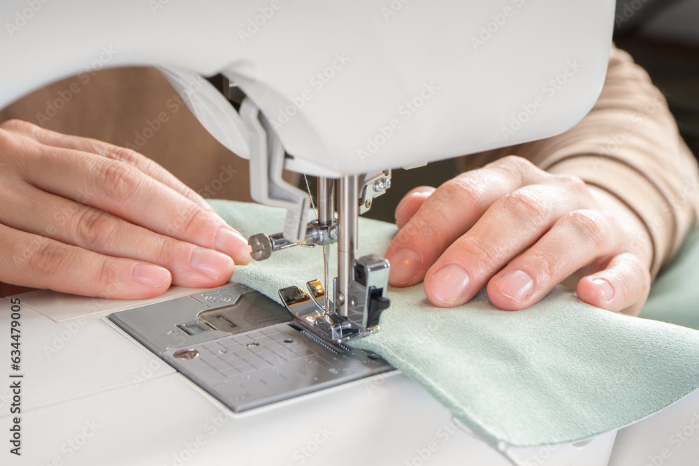 Female hands stitching green fabric on modern sewing machine at workplace in atelier. Women's hands sew pieces of fabric on a sewing machine closeup. Handmade, hobby, small business concept