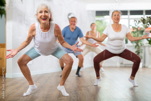 Elderly woman engaged in fitness. In dance hall of studio, she learns to perform active movements of modern youth hip hop