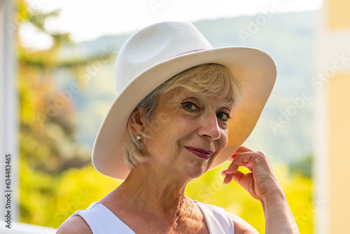 Portrait of a beautiful woman 60-70 years old in a felt white hat on a blurred background of nature. Stylish pensioner, active life of the elderly people. photo