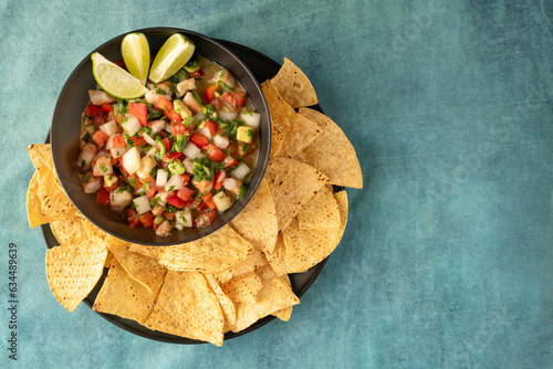 Bowl of Ceviche with lime garnish and chips on teal tablecloth with copy space