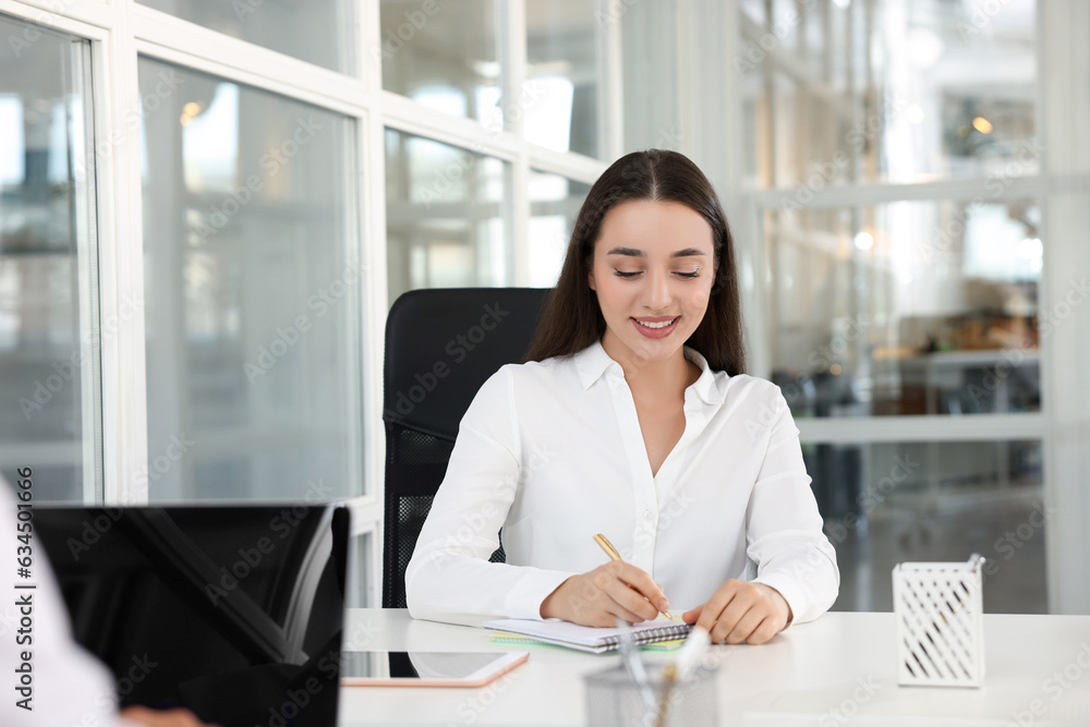 Happy woman taking notes at white desk in open plan office, space for text Happy woman taking notes at white desk in open plan office, space for text