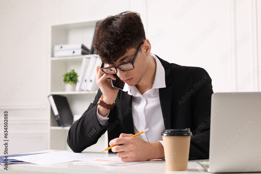 Young man talking on phone while working at table in office. Deadline concept Young man talking on phone while working at table in office. Deadline concept