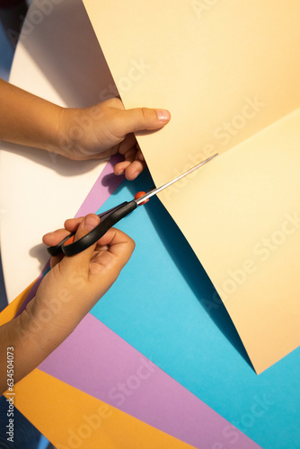 Vertical photography of a children cutting some color cupboards getting ready to be back to school. Kid making crafts with some papers and scissors.