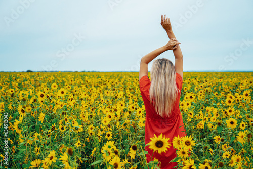 A young woman in a red dress walks through a field of sunflowers.