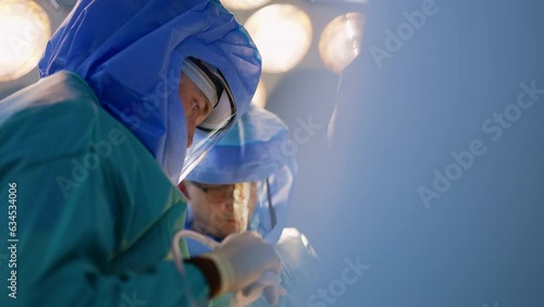 Focused faces of doctors wearing helmets in surgery room. Medics perform orthopedic operation. photo