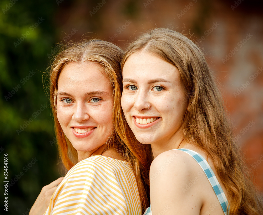 Obraz premium Young female friends outdoors in the city. They are sitting while talking at sunset in summer