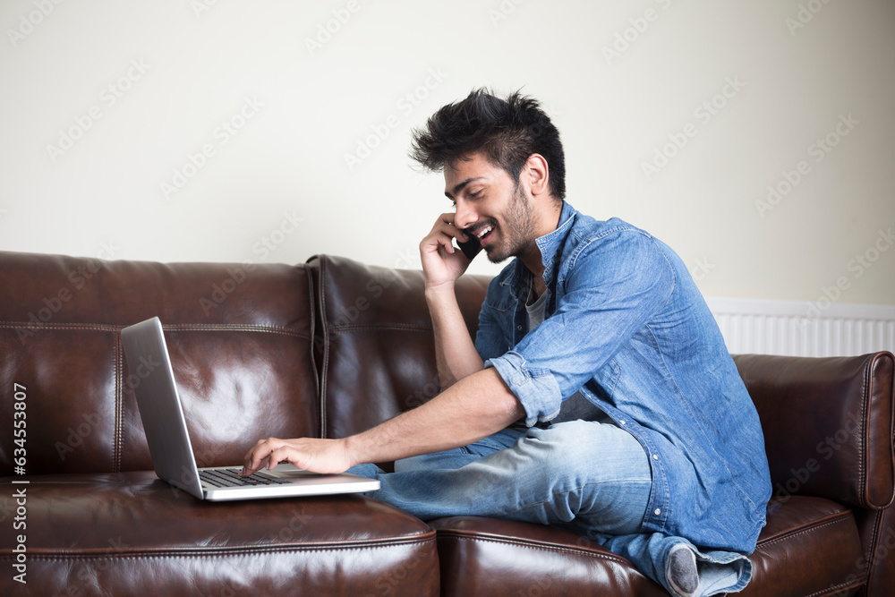 Indian Man using a laptop and phone at home.