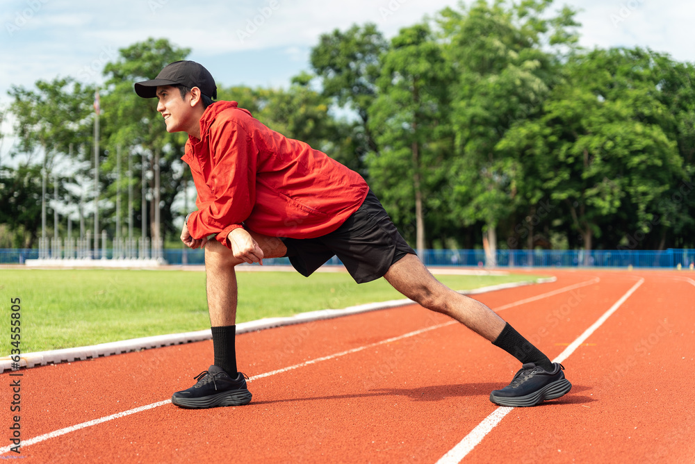 Medium shot, Young Asian man stretching his leg warm up before workout outdoor running track background. The man in sportswear exercises outside in the morning for health and wellbeing.