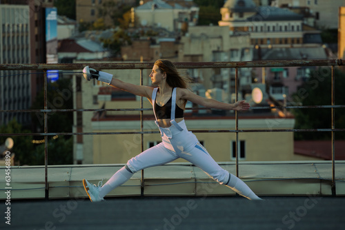 Two fencers woman practice on a rooftop with the city in the background.