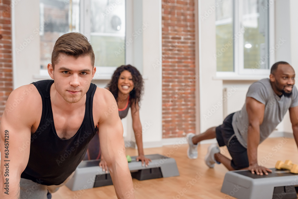 Group of happy multiethnic young friends having training in gym, Smiling faces of a varied set of people practicing push-ups in a state-of-the-art gymnasium. Group of happy multiethnic young friends having training in gym, Smiling faces of a varied set of people practicing push-ups in a state-of-the-art gymnasium.
