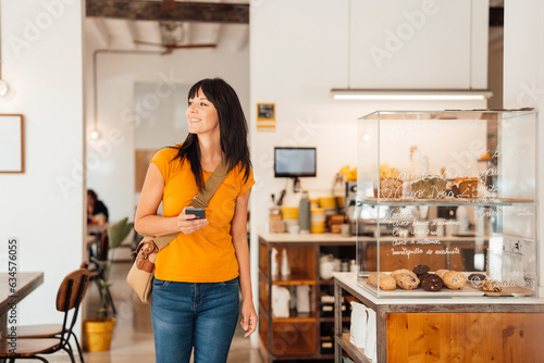 Smiling mature woman with shoulder bag and smart phone in cafe