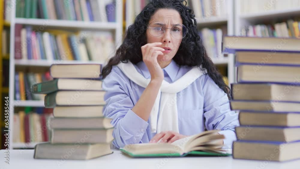 Tired female student studying by reading books in campus library space. Exhausted brunette girl learning on examination period at the university. Overworked applicant is confused and looks at camera Tired female student studying by reading books in campus library space. Exhausted brunette girl learning on examination period at the university. Overworked applicant is confused and looks at camera