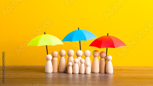 Many wooden people figures under umbrella on yellow background.