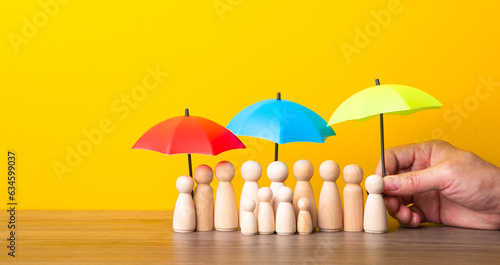 Many wooden people figures under umbrella on yellow background.