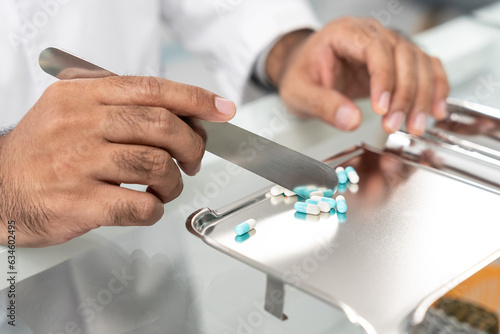 Closeup hand of male pharmacist counting and arrange pills on qualified stainless counting tray with spatula in pharmacy. Pharmacist prepare medication in stainless tray by prescription at drugstore.